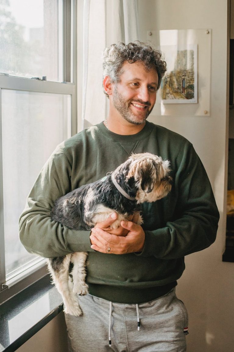 happy adult man holding purebred dog while standing near window