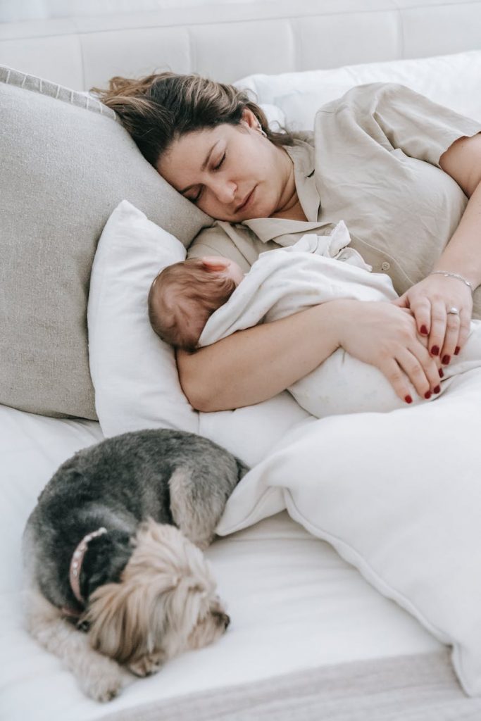 young mom with cute baby and dog sleeping on bed